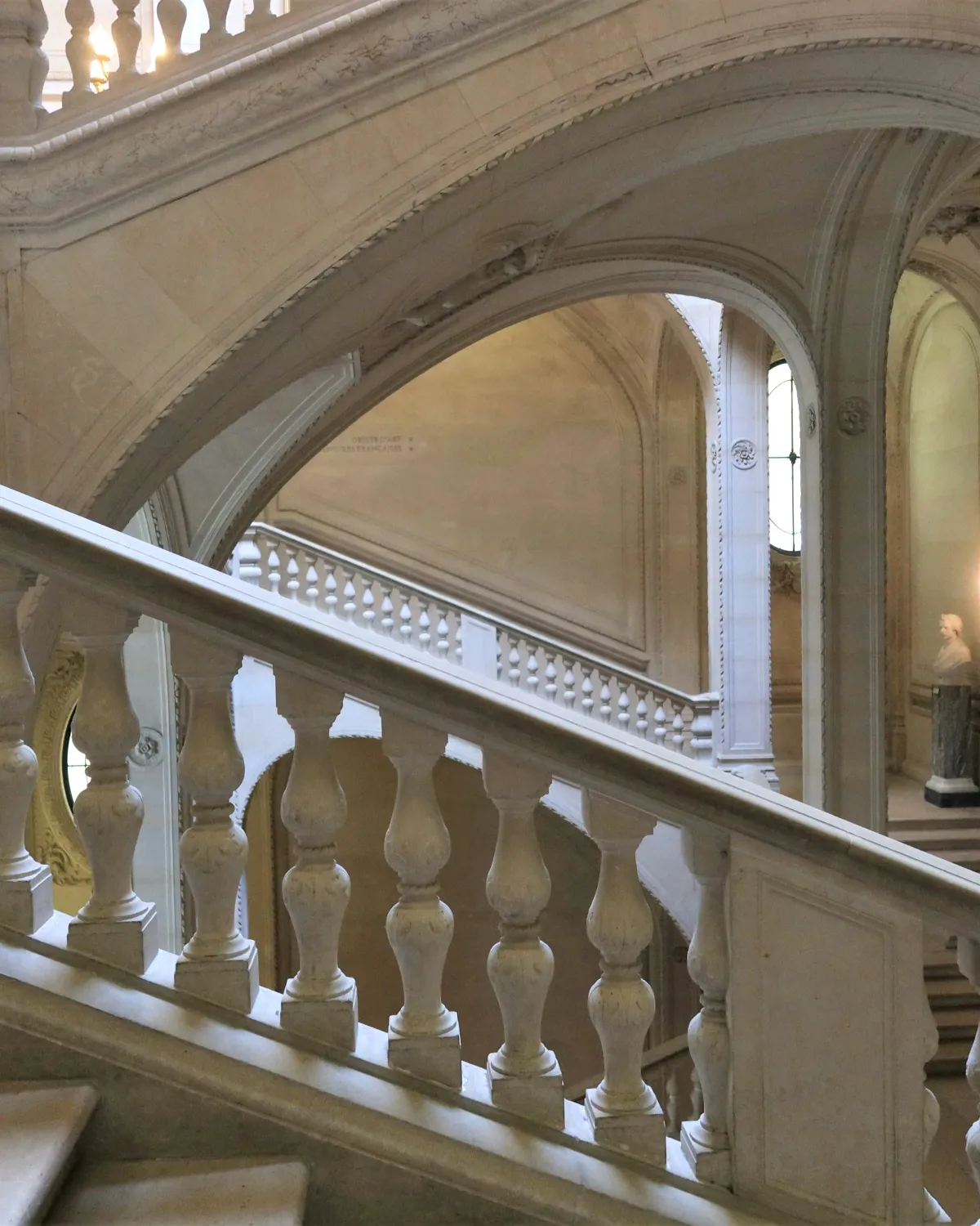 Des escaliers de marbre clair imbriqués, entre balustrades et arches de pierre